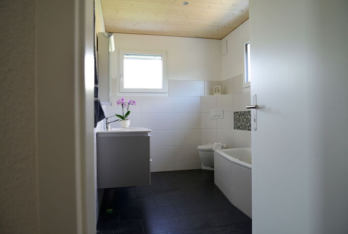 Badezimmer mit hellen Wandfliesen im Kontrast zu dunklen Bodenplatten harmonieren sehr schön mit der hellen Holzdecke