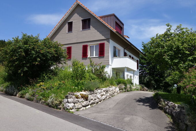 Satteldachlukarnen mit Kupfer verkleidet, rote Fensterladen passend zur grauen Holzschalung der Fassade