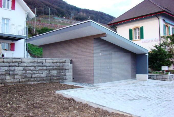 Moderne Garage mit Schrägdach und grauer Holzschalung in Kombination mit grauer Vollkernplatte