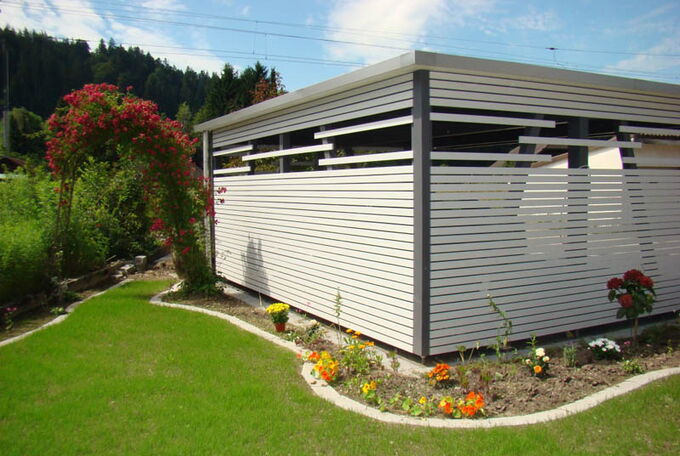 Carportansicht vom Gartensitzplatz aus, schöner und farbiger Blumengarten um den Unterstand angelegt